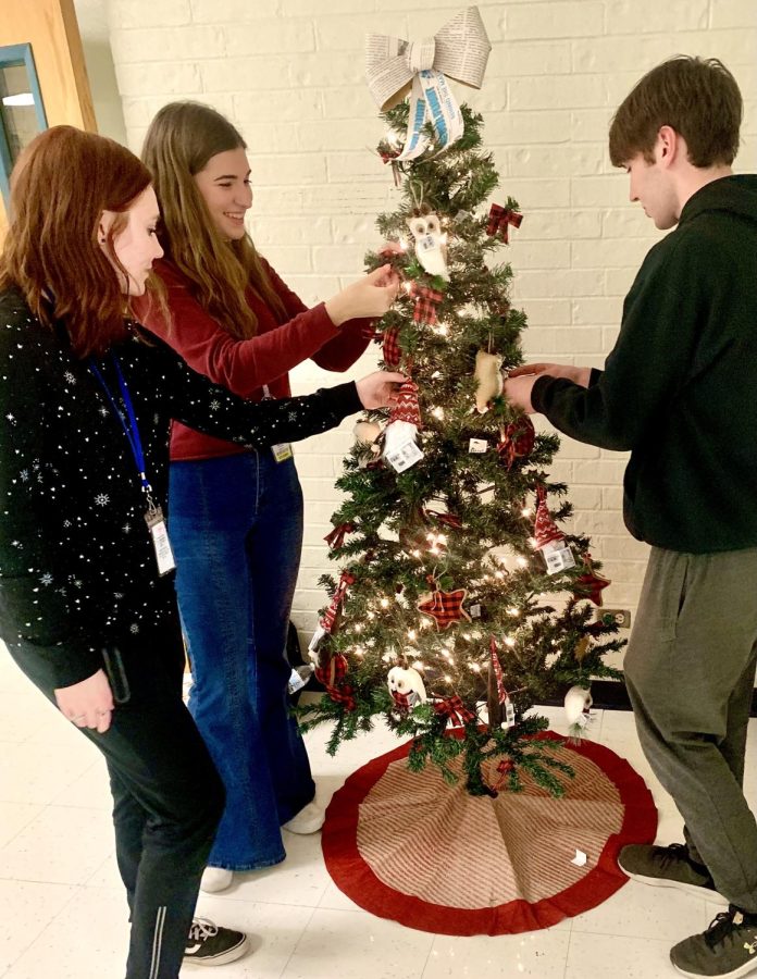 Three members of The Owl Flight Newspaper decorate their newspaper-themed tree. 